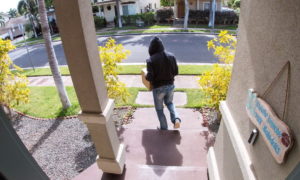 Person stealing delivery package from porch steps, surveillance camera view